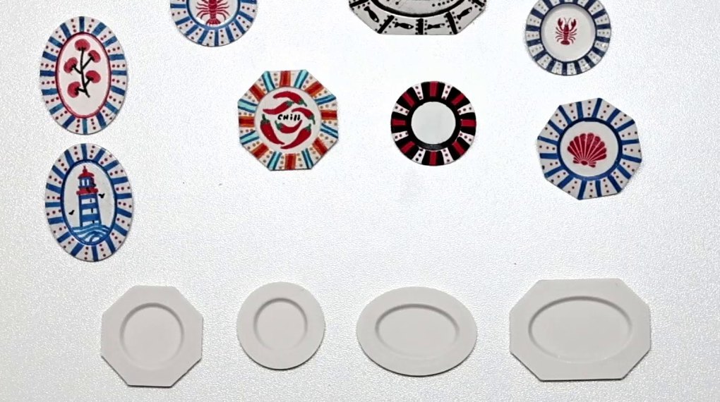 Plain white 3D printed miniature plates in four shapes, below a display of decorated plates
